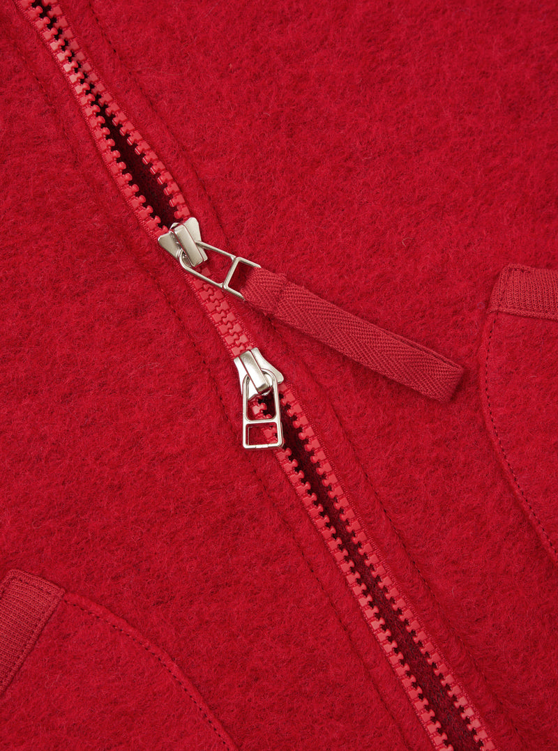 Close-up detail shot of the Scarlet Wool Fleece Zip Waistcoat on a plain background. Focuses on the metallic front zipper hardware, rounded neck trim, and vibrant scarlet red fleece texture of the garment.