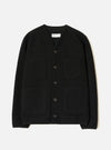 Black wool fleece cardigan laid flat on a white studio backdrop. Collarless V-neckline with a Universal Works woven label at the back neck. Five dark buttons down the centre front. Four patch pockets: two chest, two lower. Ribbed cuffs and hem. Textured fleece fabric throughout.