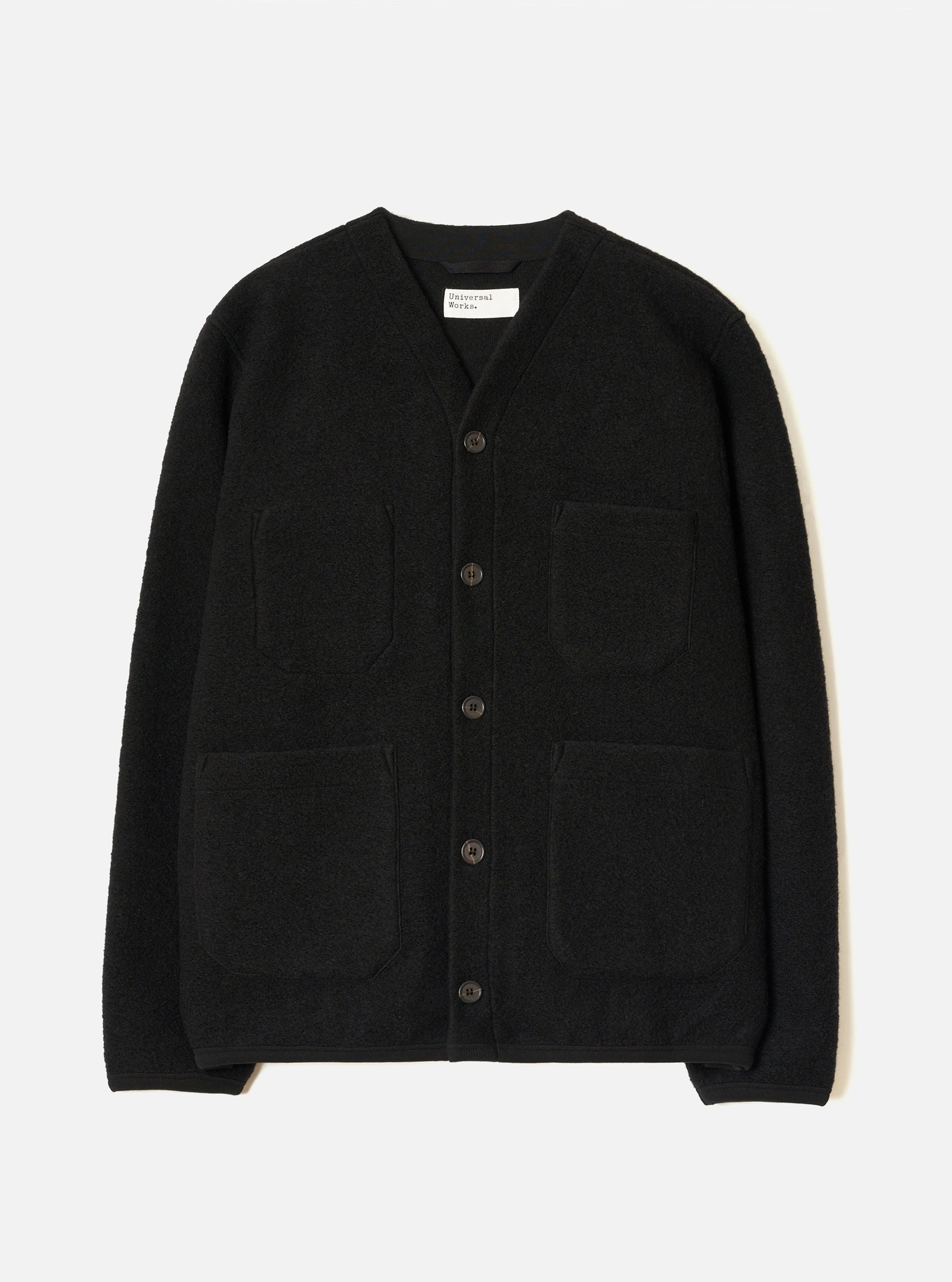 Black wool fleece cardigan laid flat on a white studio backdrop. Collarless V-neckline with a Universal Works woven label at the back neck. Five dark buttons down the centre front. Four patch pockets: two chest, two lower. Ribbed cuffs and hem. Textured fleece fabric throughout.
