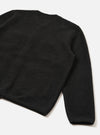 Flat lay of a black wool fleece cardigan on a white studio surface, shot from behind at an angle. The textured, fluffy fleece fabric is visible across the back panel and one full sleeve. A small tonal label sits at the upper back. The ribbed cuff is visible at the sleeve hem.