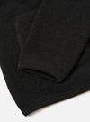 Close-up flat lay of a black wool fleece cardigan showing the sleeve cuff and lower hem. The fabric has a dense, textured fleece surface. The ribbed cuff is smooth and fitted, finished with visible stitching. The hem carries the same ribbed trim. Shot on a white studio surface.
