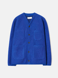 Blue wool fleece cardigan laid flat on a light grey studio backdrop. V-neckline with a branded woven label at the collar. Five dark horn buttons down the centre front. Two chest patch pockets and two larger patch pockets at the hem. Brushed wool fleece texture throughout. Straight hem and long sleeves with no cuffs.