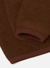 Close-up detail of a cacao brown wool fleece cardigan, flat lay on a white surface. The shot focuses on the lower sleeve and hem, showing the ribbed knit cuff and ribbed hem trim in a tonal dark burgundy-brown. The boiled wool fleece fabric has a dense, lightly brushed texture.