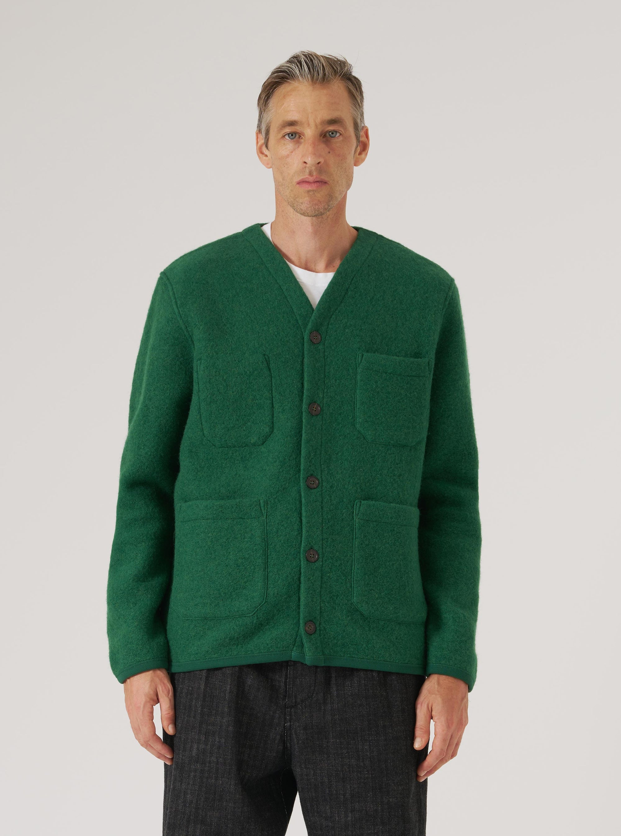 A man models a Green Wool Fleece Cardigan against a white backdrop. The cardigan has a button-up front and patch pockets. The fit is relaxed and comfortable.