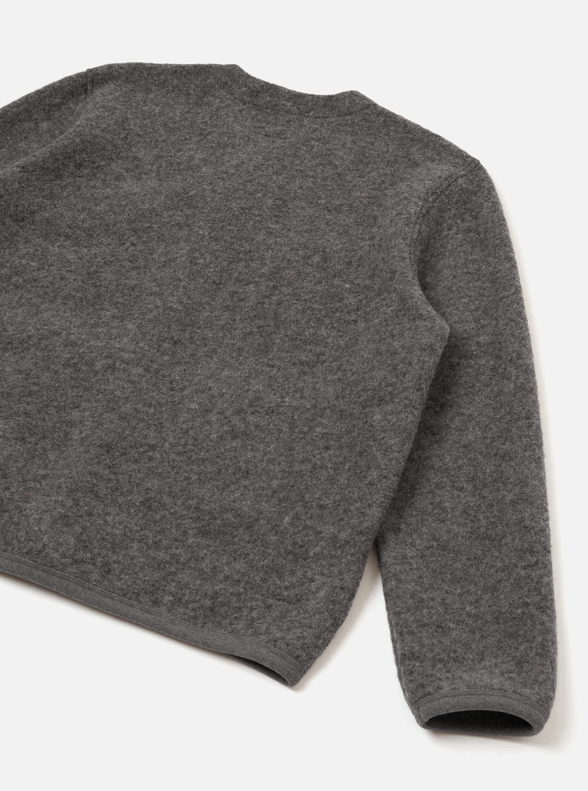Close-up flat lay of a grey marl wool fleece cardigan on a white studio surface, shot from behind and above. The boiled wool texture is clearly visible across the back panel and one full sleeve. A ribbed hem and ribbed cuff are shown at the bottom of the frame.
