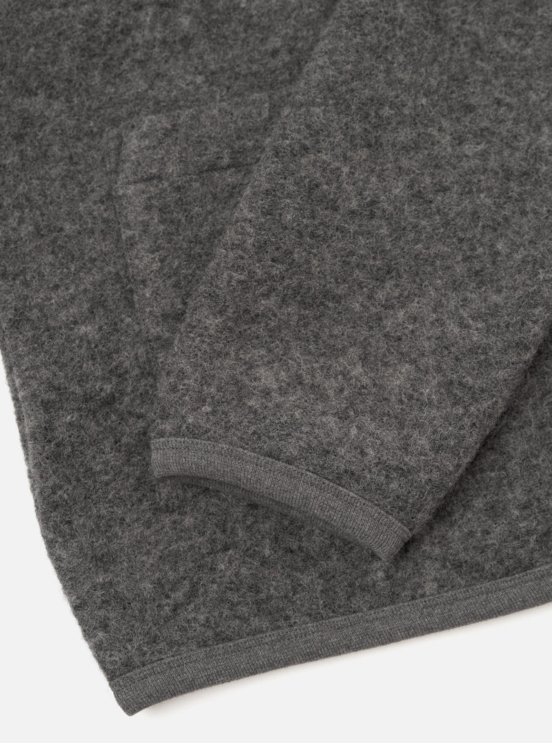 Close-up flat lay of a grey marl wool fleece cardigan on a white surface, showing the lower body and one sleeve folded back. The boiled wool texture is clearly visible across the fabric. A narrow ribbed knit hem trims the bottom edge and cuff in matching grey.