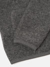 Close-up flat lay of a grey marl wool fleece cardigan on a white surface, showing the lower body and one sleeve folded back. The boiled wool texture is clearly visible across the fabric. A narrow ribbed knit hem trims the bottom edge and cuff in matching grey.