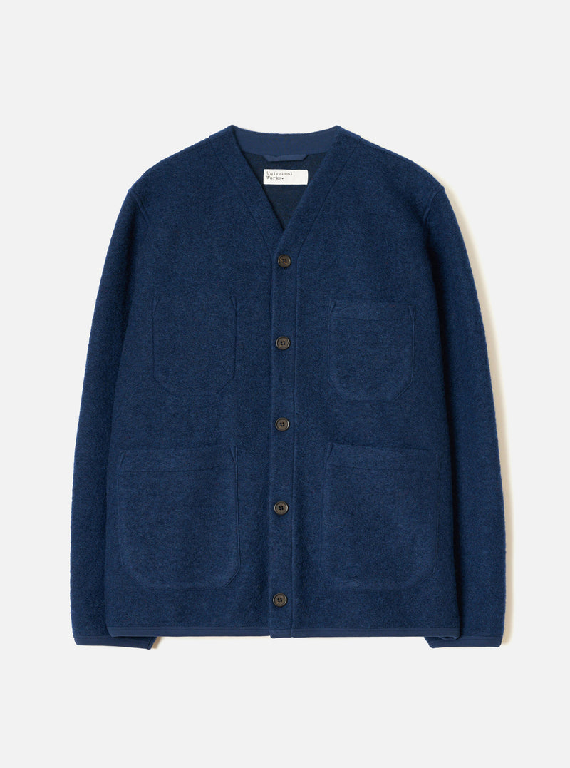 Indigo wool fleece cardigan laid flat on a light grey studio backdrop. V-neckline with a woven Universal Works label at the back neck. Five dark horn buttons down the front placket. Four patch pockets, two chest and two hip. Textured boiled wool fleece fabric. Straight hem and full-length sleeves.