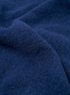 Close-up of indigo wool fleece fabric, showing a boiled or brushed texture with soft, looping fibres and a slightly felted surface. The deep navy-indigo tone is consistent across the draped folds. No garment details or background are visible.