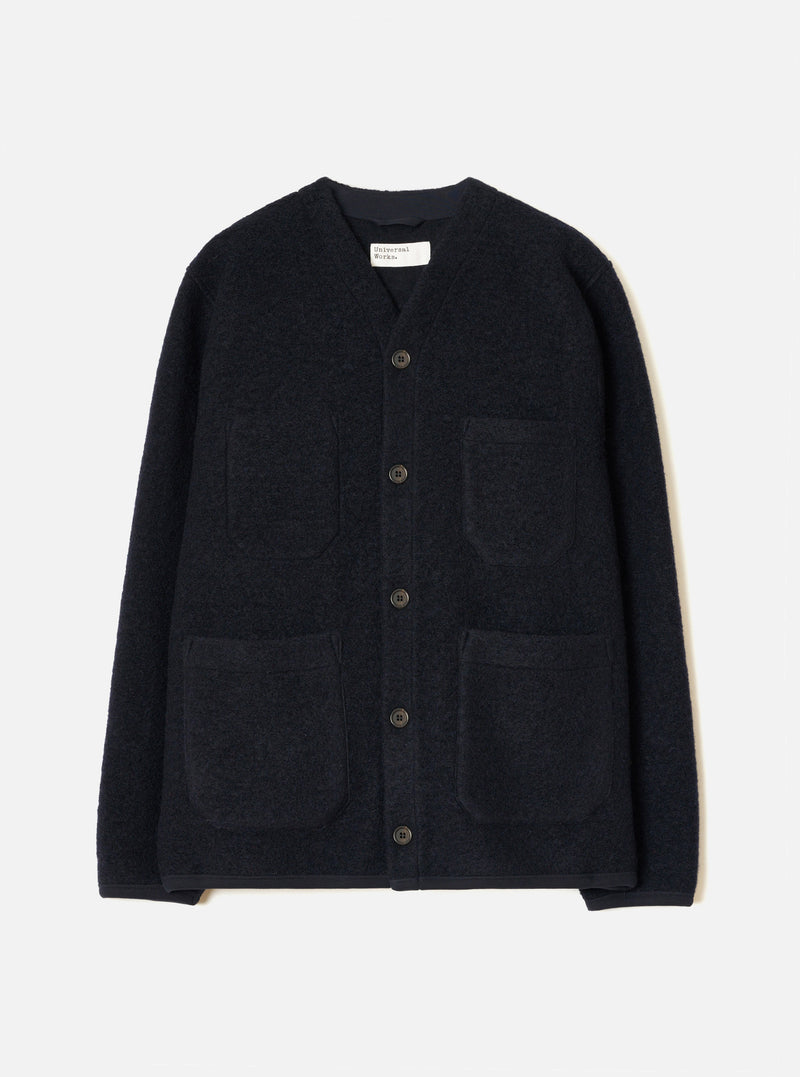 Navy wool fleece cardigan laid flat on a light grey studio backdrop. Collarless V-neckline with a woven brand label at centre back neck. Five dark buttons fasten the front placket. Four large patch pockets sit across the chest and lower front. Finished hem and cuffs in a smoother navy fabric.