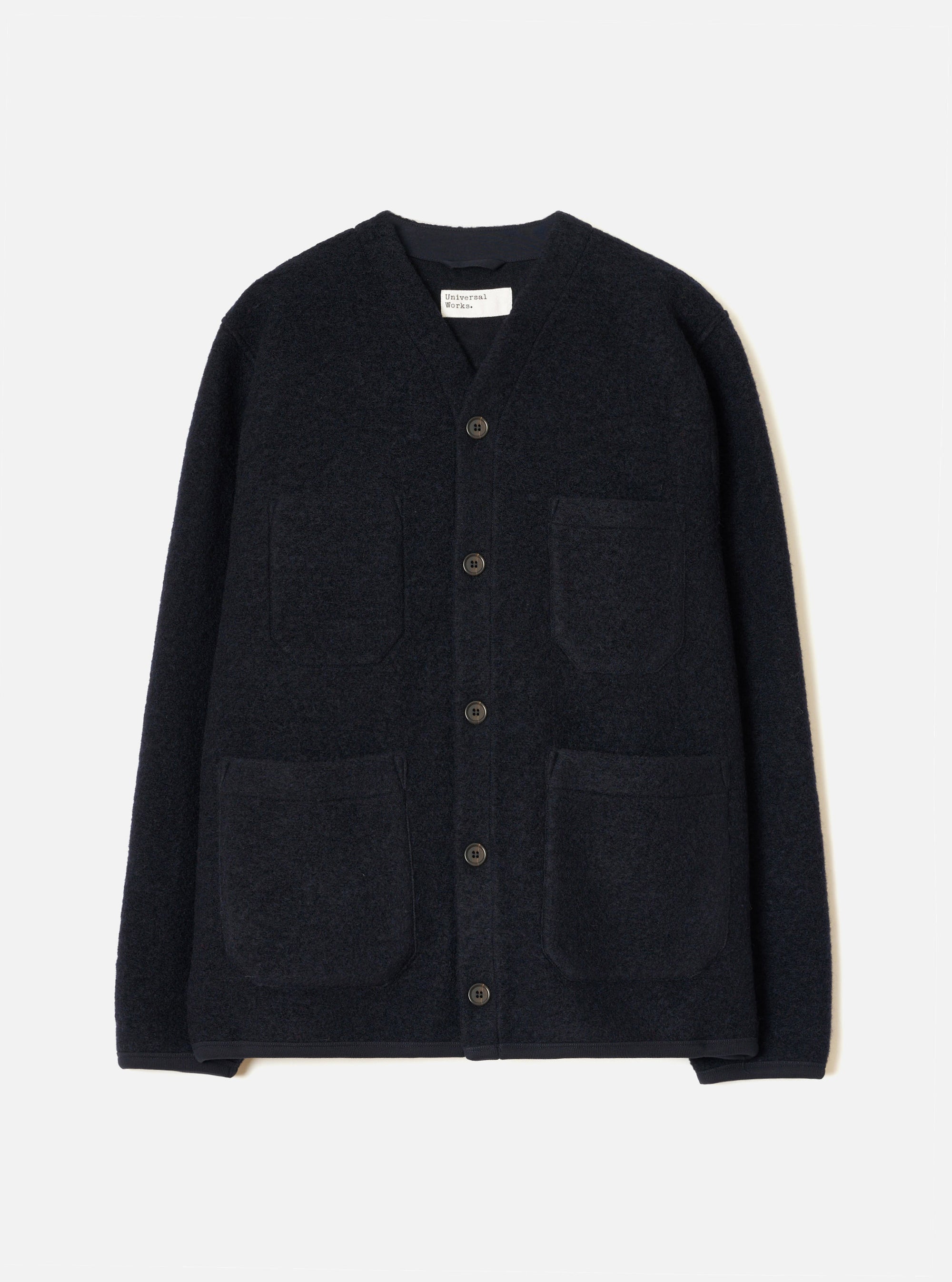 Navy wool fleece cardigan laid flat on a light grey studio backdrop. Collarless V-neckline with a woven brand label at centre back neck. Five dark buttons fasten the front placket. Four large patch pockets sit across the chest and lower front. Finished hem and cuffs in a smoother navy fabric.