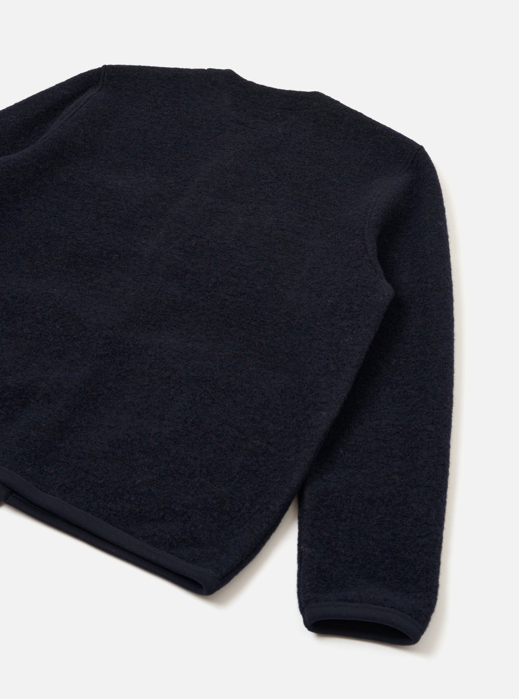 Navy wool fleece cardigan laid flat on a white surface, shot at an angle showing the back and one sleeve. The textured fleece has a dense, nubby surface. A ribbed cuff is visible at the sleeve end, with a clean bound hem at the base.