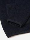 Close-up flat lay of a navy wool fleece cardigan on a white surface, showing the sleeve cuff and hem. The boiled wool texture is visible across the fabric. Both the ribbed cuff and straight hem are finished with a narrow dark navy grosgrain ribbon trim.