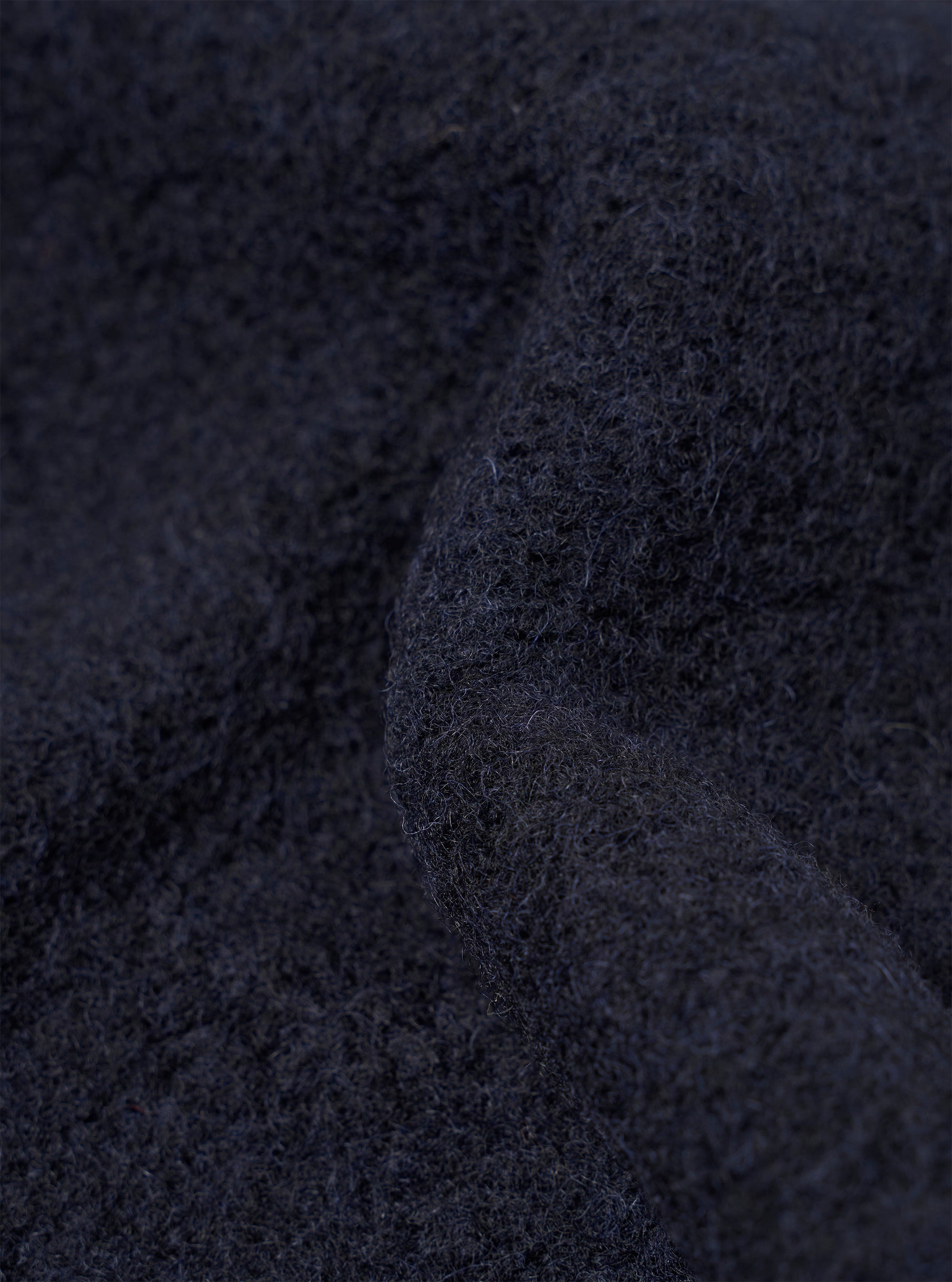 Close-up fabric detail of a navy wool fleece cardigan, showing the dense, brushed texture with fine raised fibres across the surface. The deep navy tone and fluffy knit construction are clearly visible. No background is distinguishable in this macro shot.