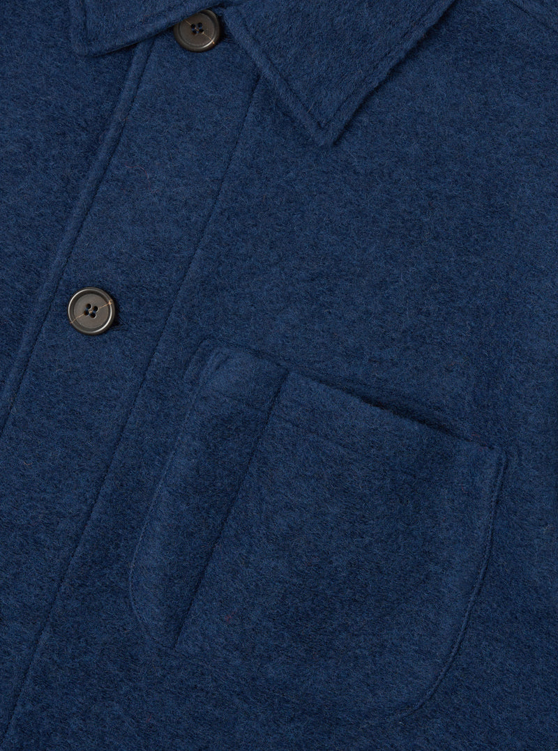 Detailed close-up shot of the Indigo Wool Fleece Field Jacket on a white backdrop. Focuses on the textured wool fleece material, fine stitching, button placket, and flap pocket construction.