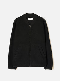 Black wool fleece zip bomber jacket, flat lay on a light grey seamless backdrop. Ribbed bomber collar with a Universal Works label visible at the neckline. Full-length silver zip with a leather pull tab. Textured boiled wool fleece body, two front welt pockets, and ribbed cuffs at the hem of each sleeve.