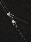 Close-up detail of the double zip fastening on a black wool fleece bomber jacket. Two silver-toned zip sliders sit on black chunky zip teeth, with the zip partially open to reveal a woven black storm placket beneath. The boiled wool fleece texture is clearly visible across the charcoal-black fabric.