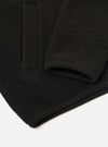 Close-up flat lay of a black wool fleece zip bomber on a white surface. The shot focuses on the lower sleeve and hem, showing the ribbed knit cuff and ribbed hem band. The dense, textured wool fleece fabric is visible in detail across the body and sleeve.