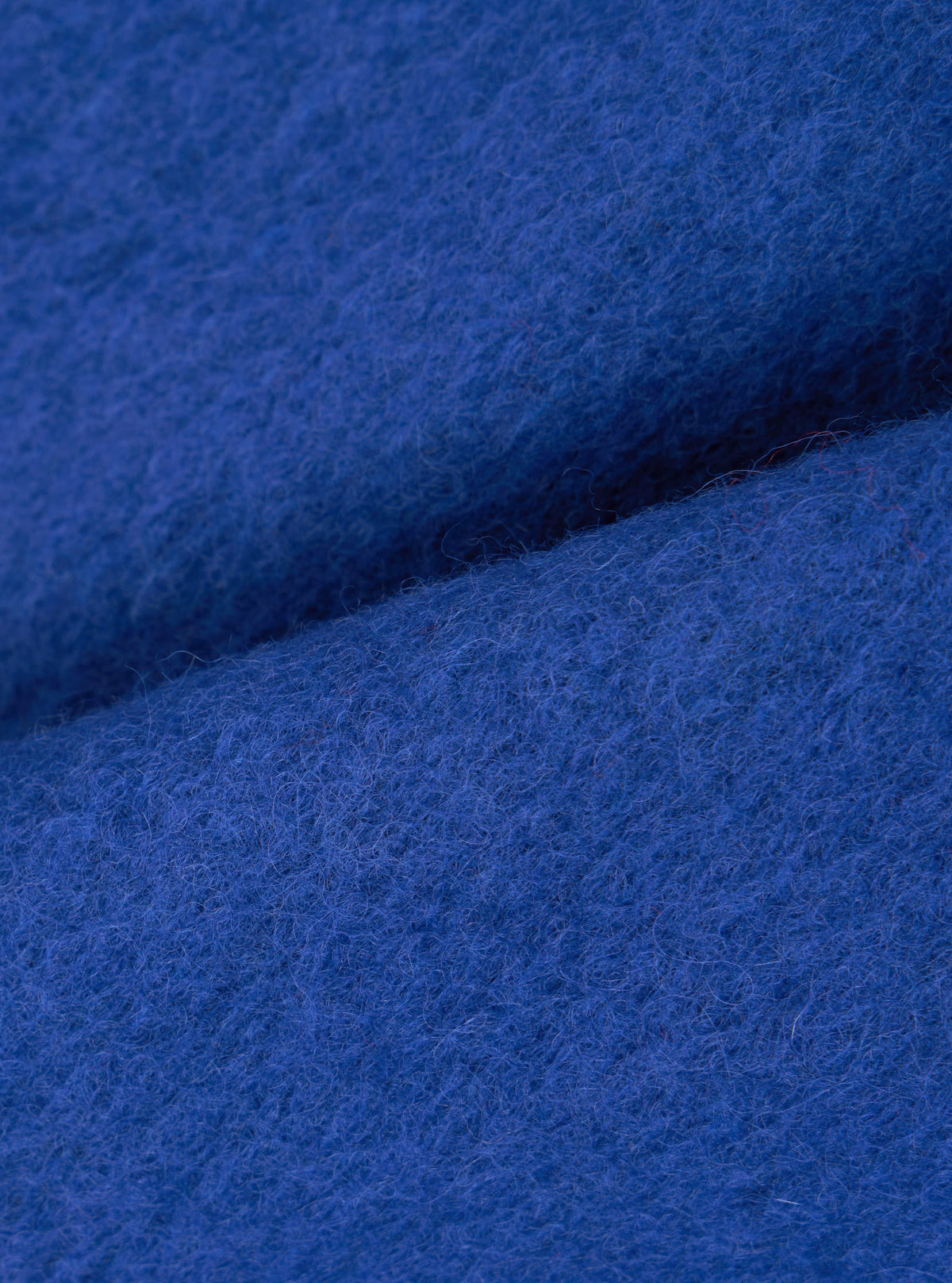 Close-up of the cobalt blue wool fleece fabric used in the zip bomber, showing the dense, lightly boiled texture with fine loose fibres on the surface. The fabric is folded to reveal its soft, brushed face and substantial weight. No garment details are visible.