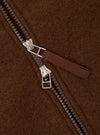 Close-up detail of the double zip on a cacao wool fleece bomber. Two gunmetal zip sliders with silver hardware sit mid-track on a dark resin chain. A woven fabric zip pull in deep burgundy-brown is attached to the upper slider. The brushed wool fleece ground shows a dense, hairy texture throughout.