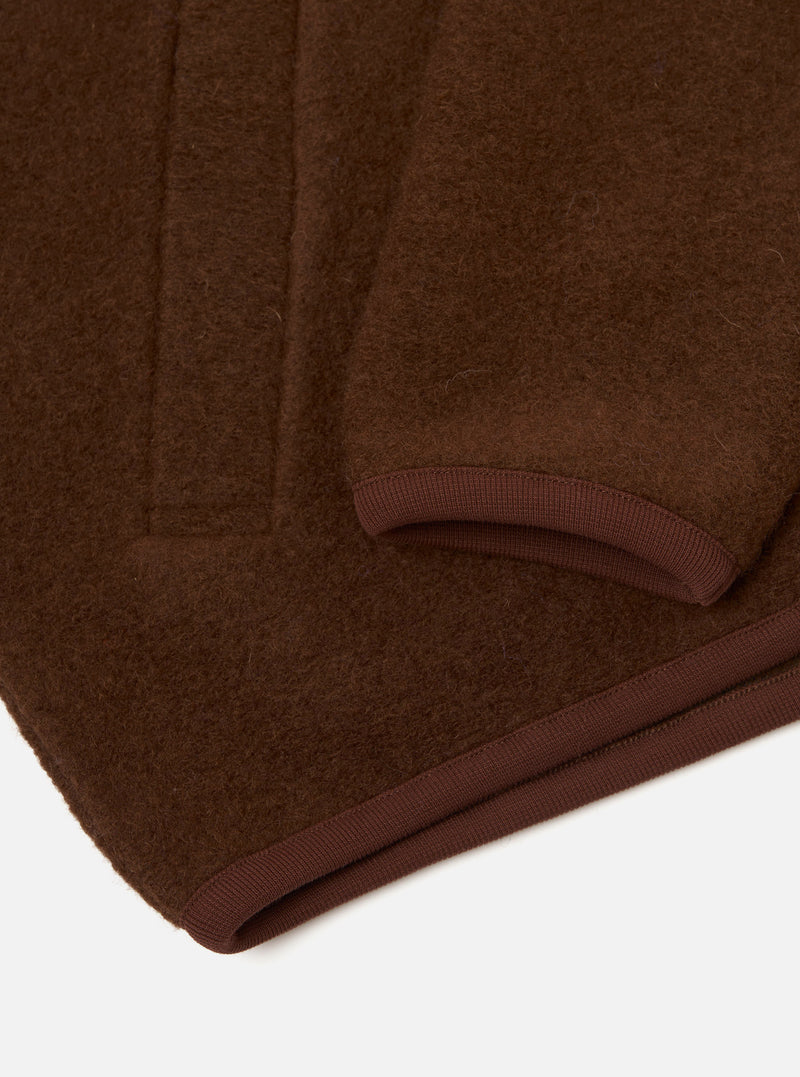 Close-up flat lay of a cacao wool fleece zip bomber on a white surface, showing the hem and sleeve cuff. The brushed wool fleece has a dense, slightly napped texture. A darker brown ribbed knit trim edges both the curved cuff opening and the straight hem. Vertical fold lines are visible across the body of the garment.
