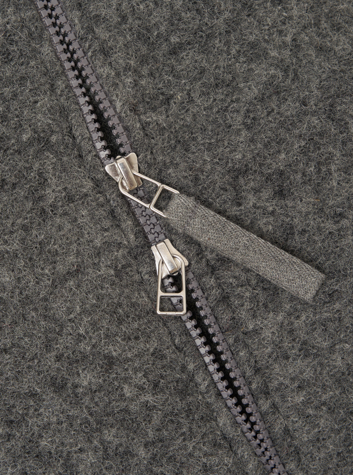 Close-up detail of the grey marl wool fleece zip bomber, showing a two-way gunmetal zip with twin silver-toned sliders and a woven fabric zip garage. The brushed wool fleece texture is visible across the full frame, showing a flecked marl finish.