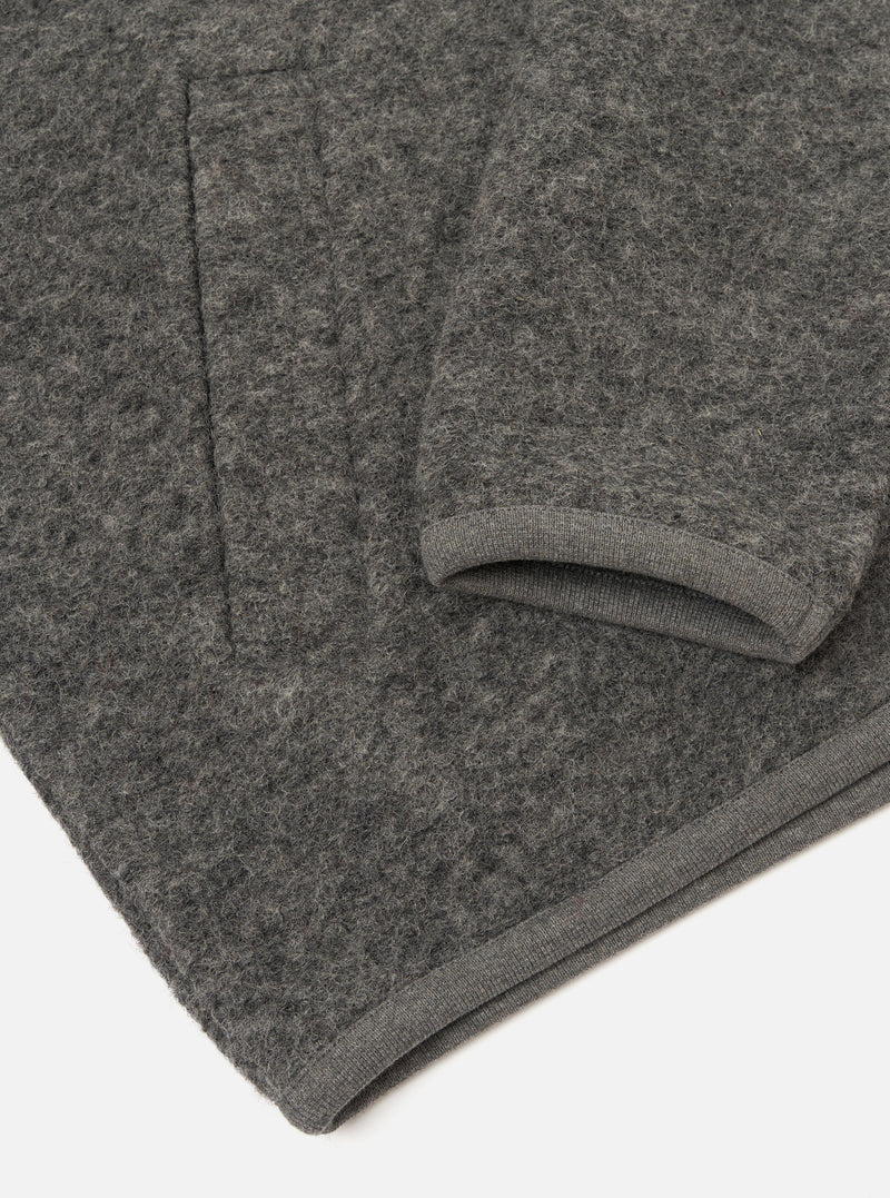Close-up flat lay of a grey marl wool fleece zip bomber, folded to show the sleeve and hem. The boiled wool fleece has a dense, nubby texture throughout. A ribbed knit cuff is visible at the sleeve end, and a matching ribbed hem strip runs along the bottom edge. Shot on a white studio surface.