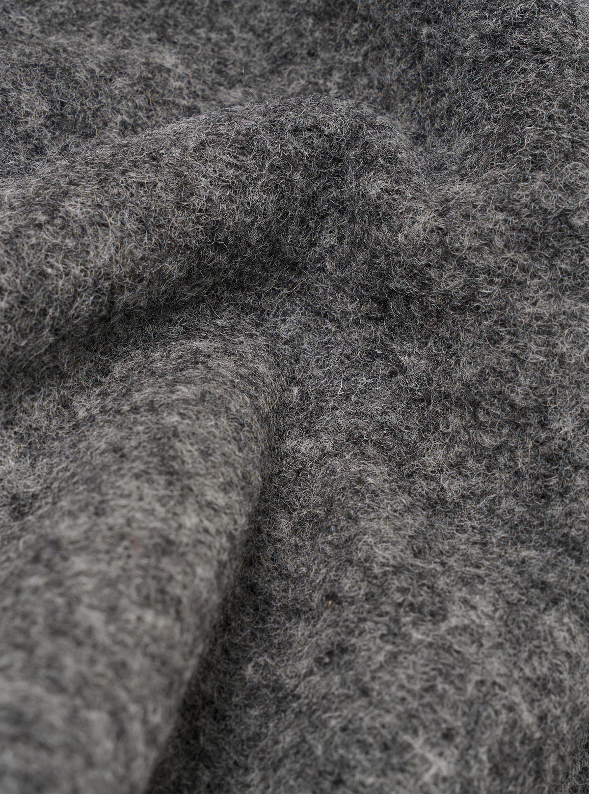 Close-up detail shot of the grey marl wool fleece fabric, showing the dense, brushed texture with fine fibres and a slightly bobbly surface. Soft folds and curves of the material fill the entire frame, highlighting the midtone charcoal colour and tactile depth of the fleece.