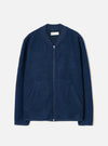 Indigo wool fleece zip bomber laid flat on a light grey studio backdrop. The jacket features a ribbed bomber collar in matching navy fabric, a full-length silver zip, two welt hip pockets, and ribbed cuffs. The boiled wool fleece has a dense, textured surface. A Universal Works woven label is visible at the neck.
