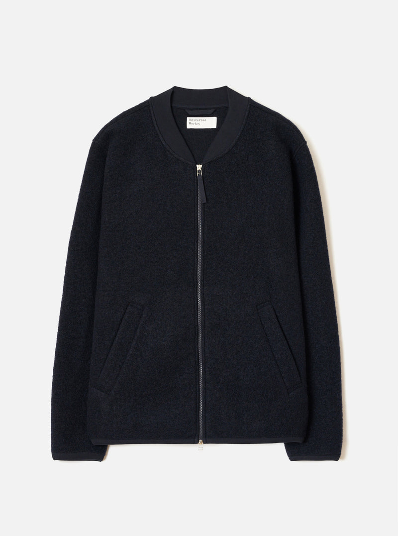 Navy wool fleece zip bomber jacket, flat lay on a light grey seamless backdrop. Textured boiled-wool-style fleece body with a smooth ribbed bomber collar in contrast navy fabric. Full-length silver zip with a small pull tab. Two welt pockets at the hip. Ribbed cuffs and hem. Universal Works woven label visible at the back neck.