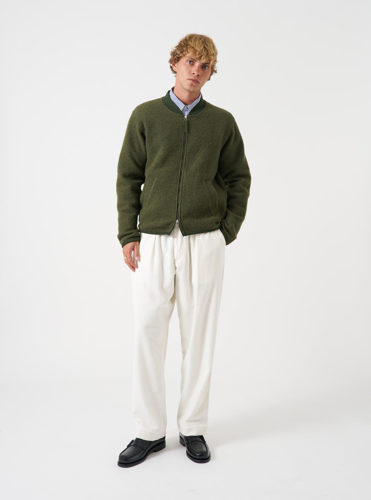 Front view of a model wearing the Olive Wool Fleece Zip Bomber Jacket in a light studio backdrop. The model faces forward, showing the olive green wool fleece jacket, full zip closure, ribbed cuffs, and collar.