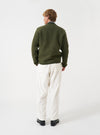 Angled view of a model wearing the Olive Wool Fleece Zip Bomber Jacket in a plain studio setting. Demonstrates the garment side profile, olive green wool fleece texture, full zipper, and comfortable bomber fit.