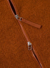 Close-up of the rust-colored Wool Fleece Zip Bomber, showcasing the texture and zipper detail. The background is a simple, clean surface.
