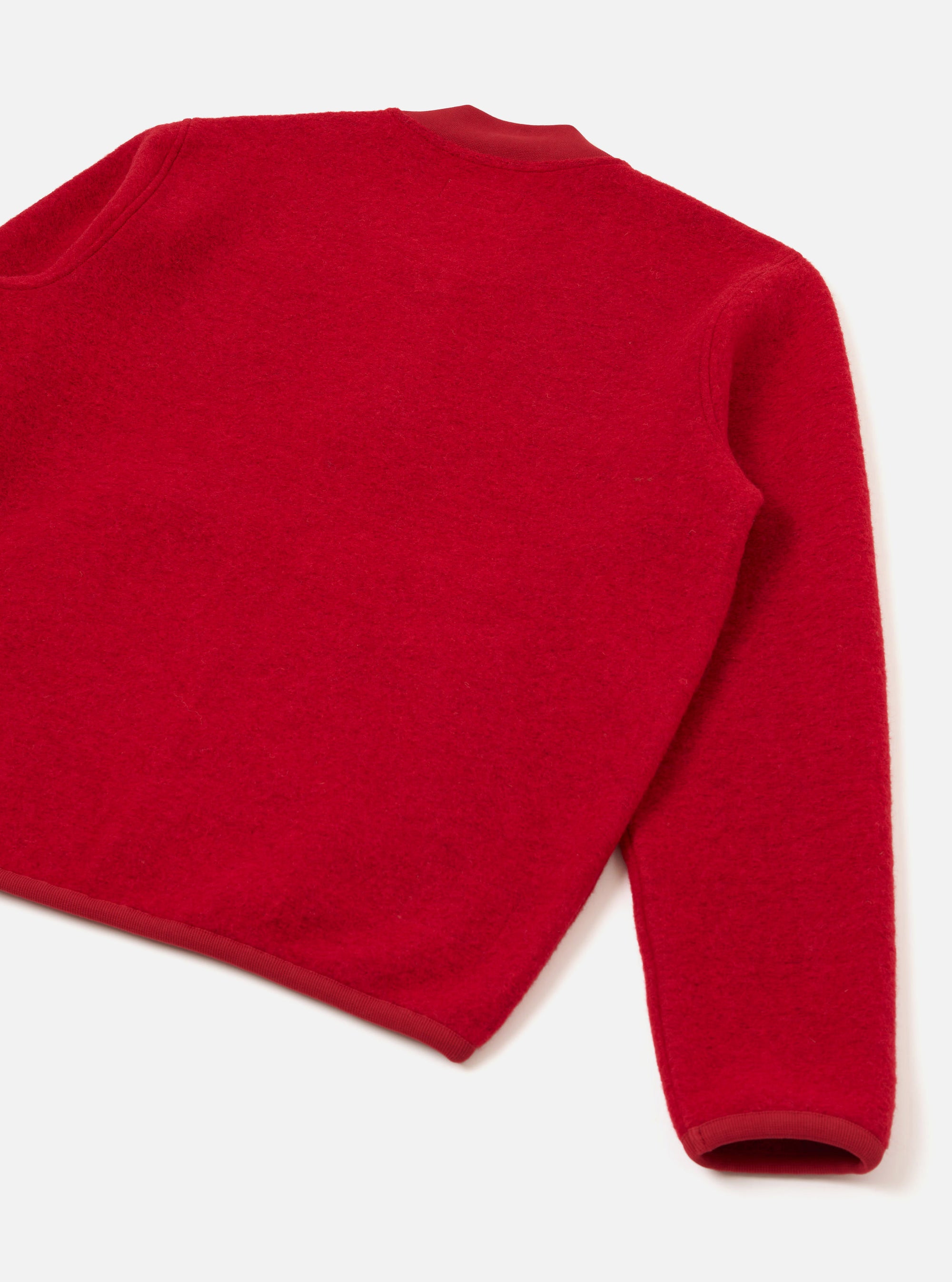 Scarlet wool fleece zip bomber shot flat on a white studio surface, angled to show the back and one sleeve. The boiled wool texture is visible across the body. A tonal satin ribbon trims the crew neckline, hem and cuff. No zip or collar visible from this angle.