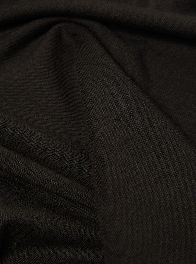 Close-up of the Black Single Jersey Core Tee fabric. The soft, single jersey material is draped to show texture. Dark, neutral background.