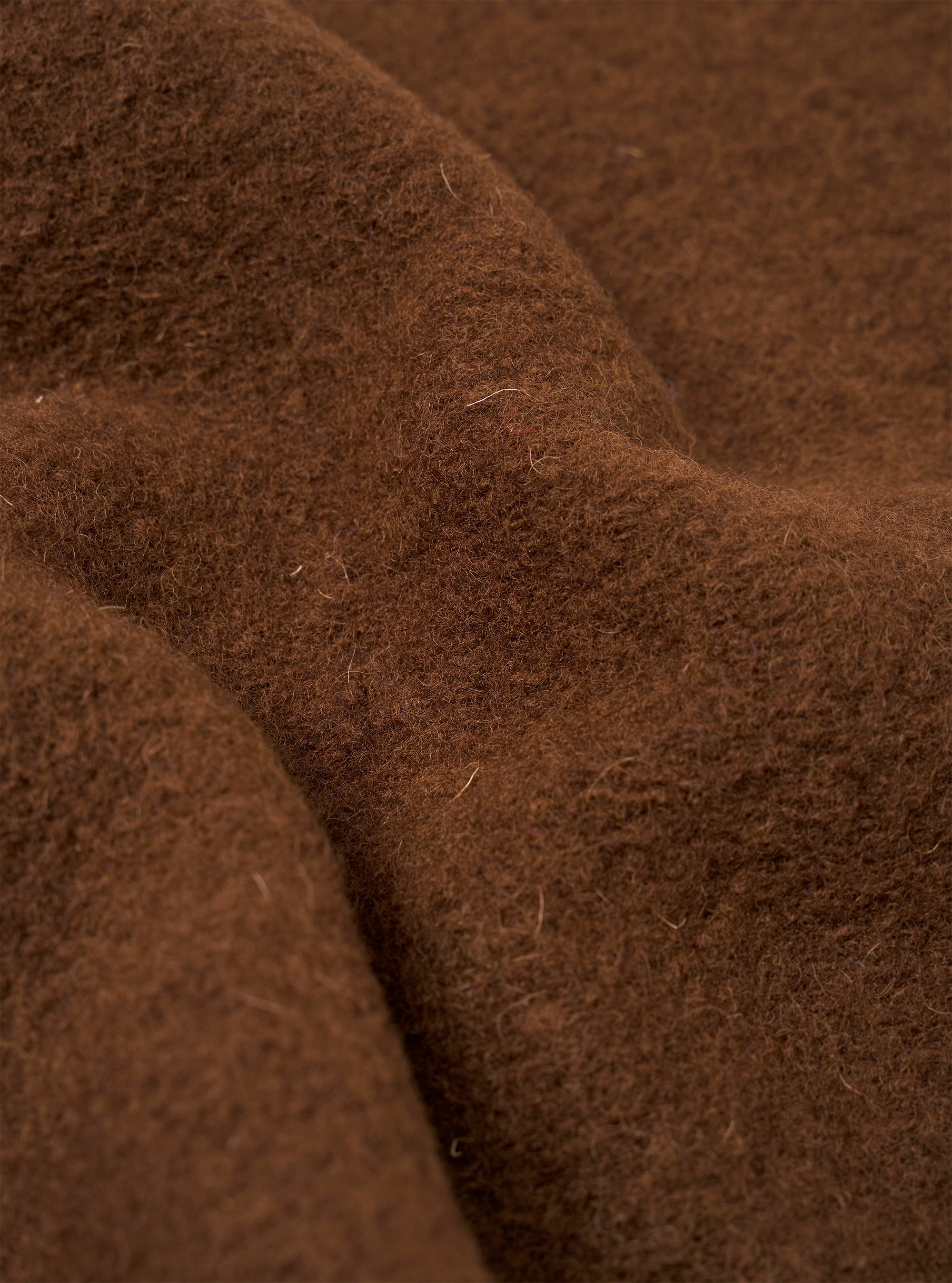 Close-up detail shot of the cacao wool fleece fabric used in the zip liner jacket. The texture shows a dense, brushed surface with visible individual fibres in a warm brown tone. Soft folds in the fabric highlight the plush, fluffy pile and the depth of the fleece.