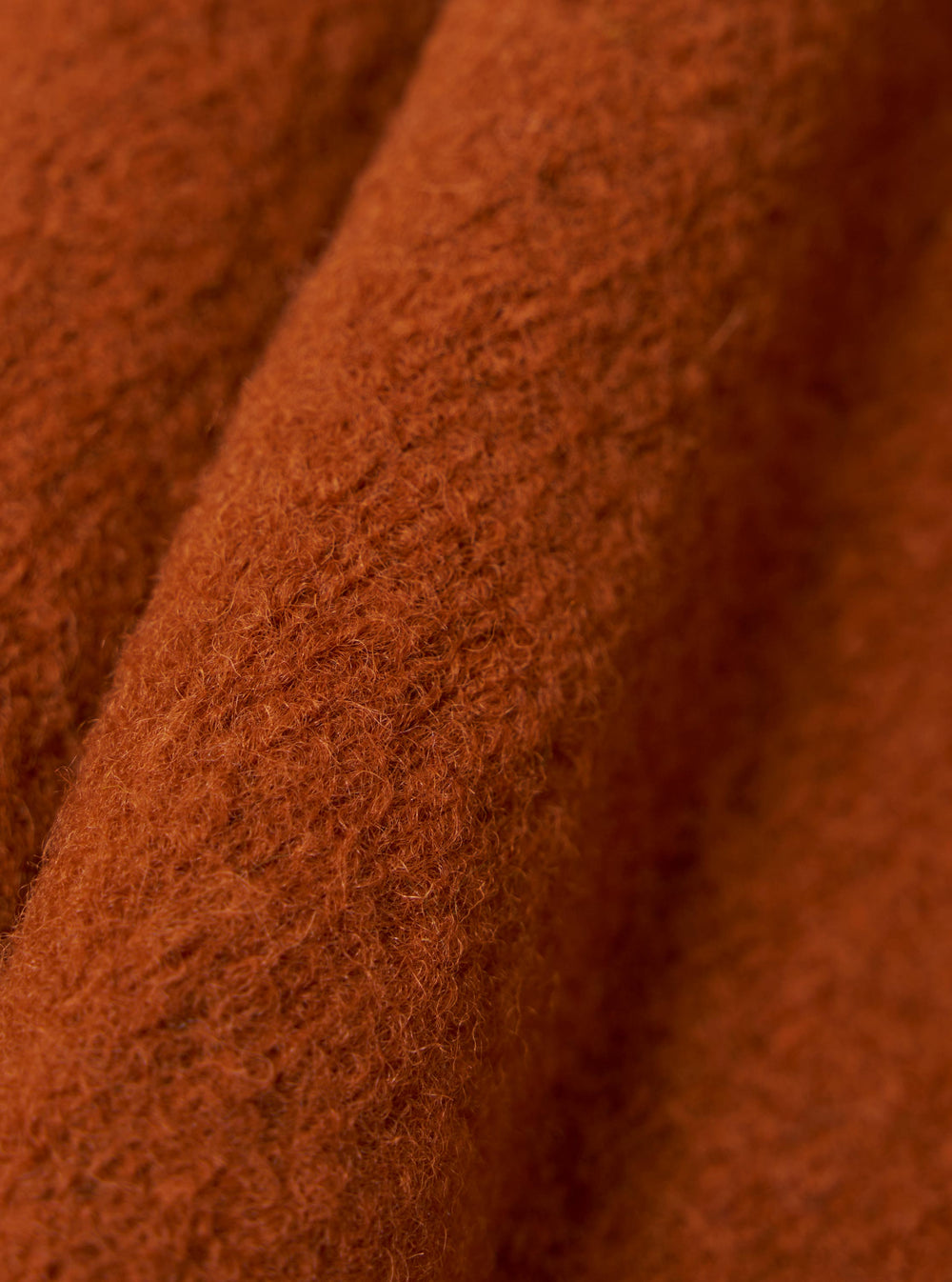 Close-up of the rust-colored Wool Fleece Zip Liner Jacket. The soft, textured wool is draped to show its warmth and quality. The background is a simple, neutral surface.