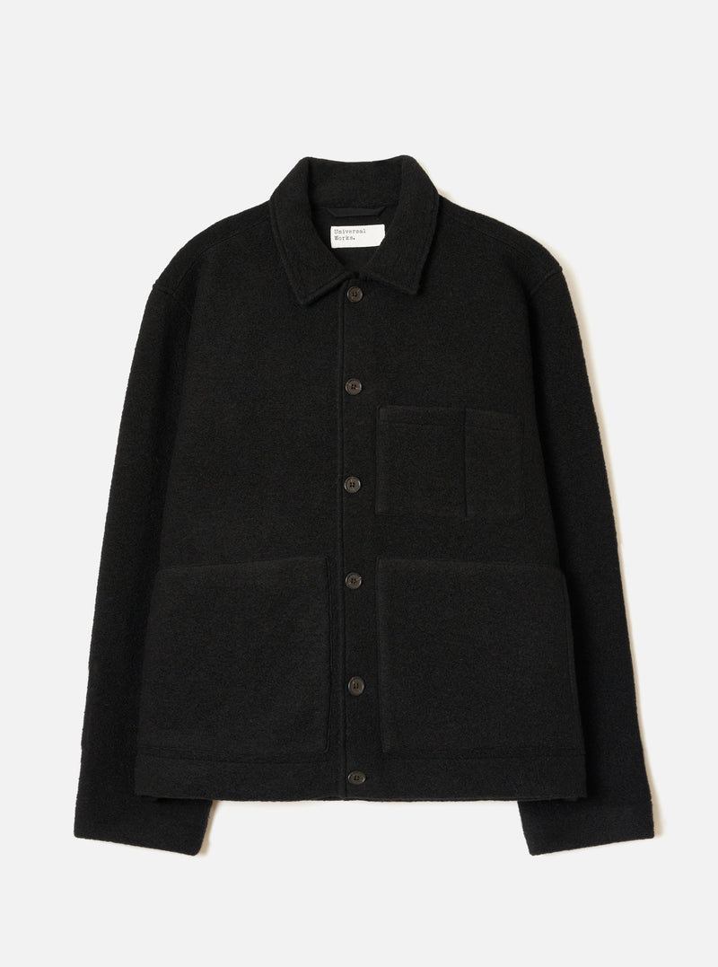Black wool fleece uniform jacket laid flat on a white studio backdrop. Features a point collar, five dark buttons down the centre front, one chest patch pocket and two large lower patch pockets. The textured boiled wool fleece fabric is visible throughout. A Universal Works woven label sits inside the collar.