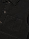 Close-up of a black wool fleece uniform jacket showing the point collar, buttoned placket with dark four-hole buttons, and a large patch chest pocket with an internal divider seam. The brushed fleece texture is clearly visible. No model or mannequin present. Plain dark studio backdrop.