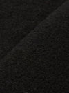 Close-up fabric detail of the black wool fleece uniform jacket, showing the dense, nubby texture with fine looped fibres across the surface. A folded seam or edge runs diagonally through the frame, highlighting the fabric's depth and weight.
