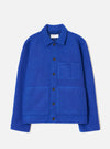 Blue wool fleece uniform jacket laid flat on a light grey studio backdrop. Features a point collar with a Universal Works label, a five-button front placket with dark brown buttons, one chest patch pocket, two large lower patch pockets, and ribbed cuffs. The boiled wool texture is visible throughout.