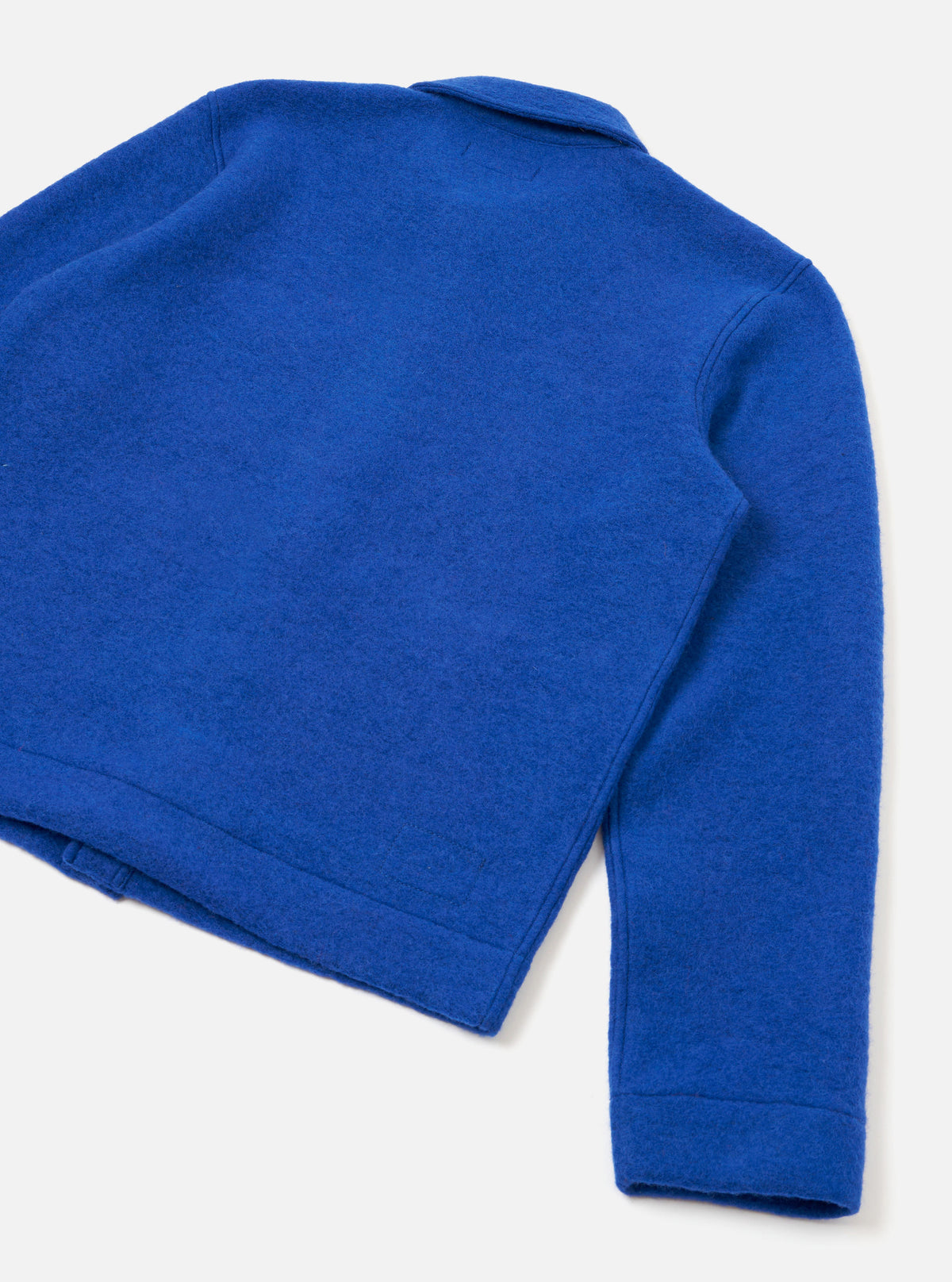 Rear three-quarter flat lay of a blue wool fleece uniform jacket on a light grey backdrop. The boiled wool texture is visible across the back panel. A small collar is partially visible at the top. The sleeve extends to the lower right, finished with a plain ribbed cuff. The straight hem features a topstitched band.