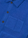 Close-up of a blue wool fleece uniform jacket shot flat against a white background. The shot focuses on the chest, showing a point collar, a button placket with dark horn-style buttons, and a square patch pocket on the left chest with topstitched edges. The fabric has a dense, brushed texture.
