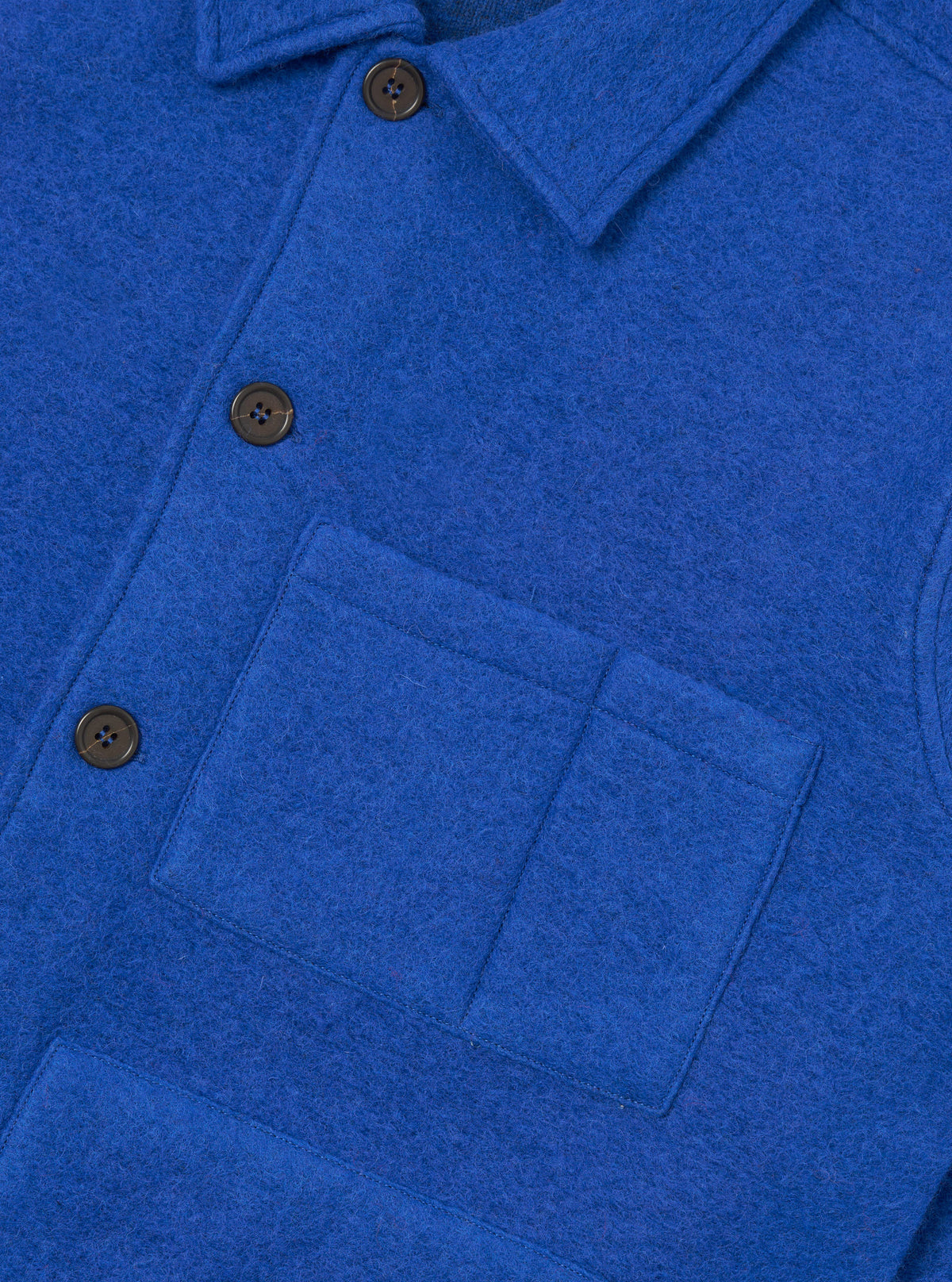 Close-up of a blue wool fleece uniform jacket shot flat against a white background. The shot focuses on the chest, showing a point collar, a button placket with dark horn-style buttons, and a square patch pocket on the left chest with topstitched edges. The fabric has a dense, brushed texture.