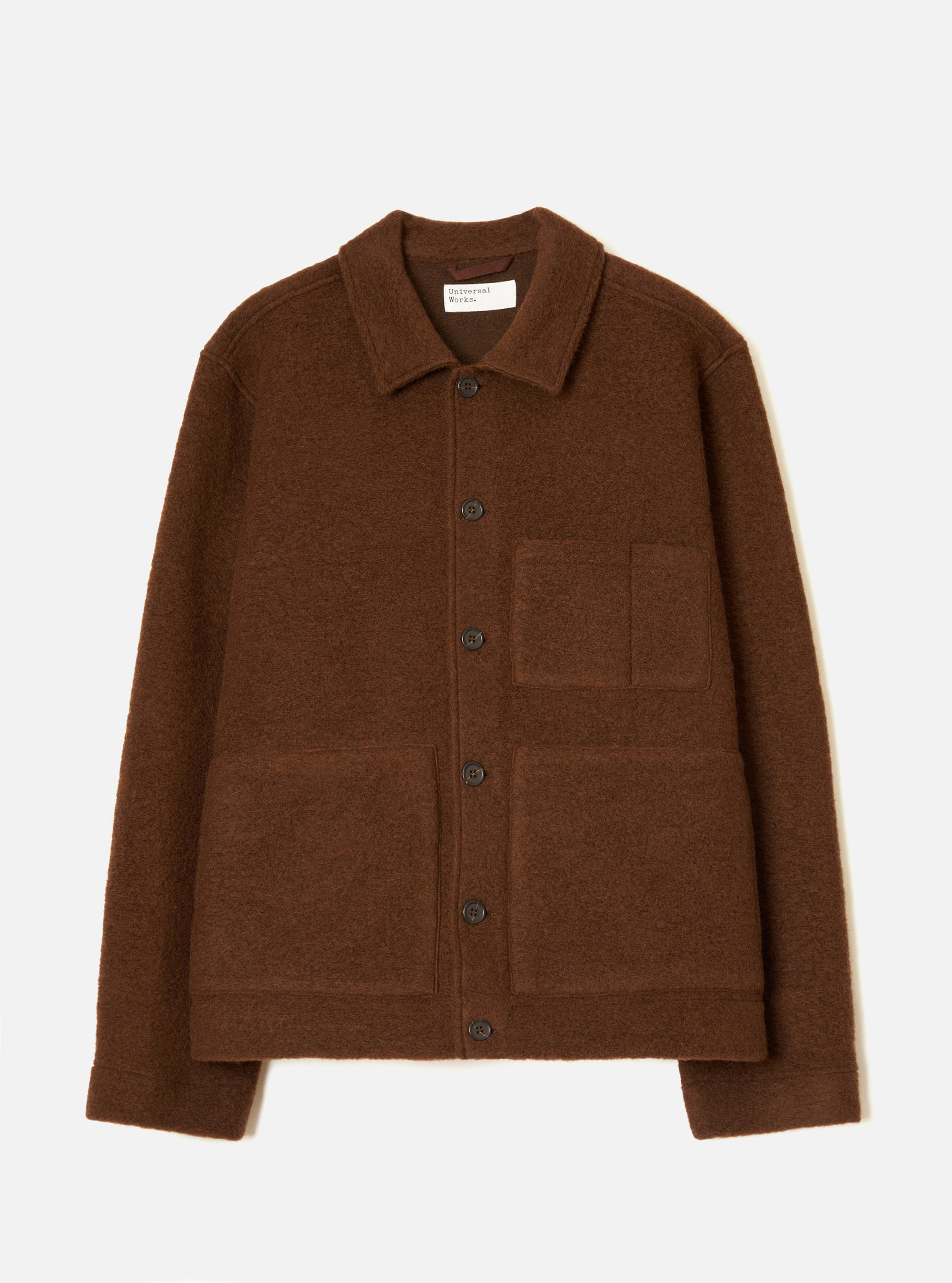 Cacao brown wool fleece uniform jacket laid flat on a light grey studio backdrop. Features a spread collar with a Universal Works woven label, a single-breasted button placket with six dark buttons, one chest patch pocket, two large lower patch pockets, and ribbed cuffs and hem.
