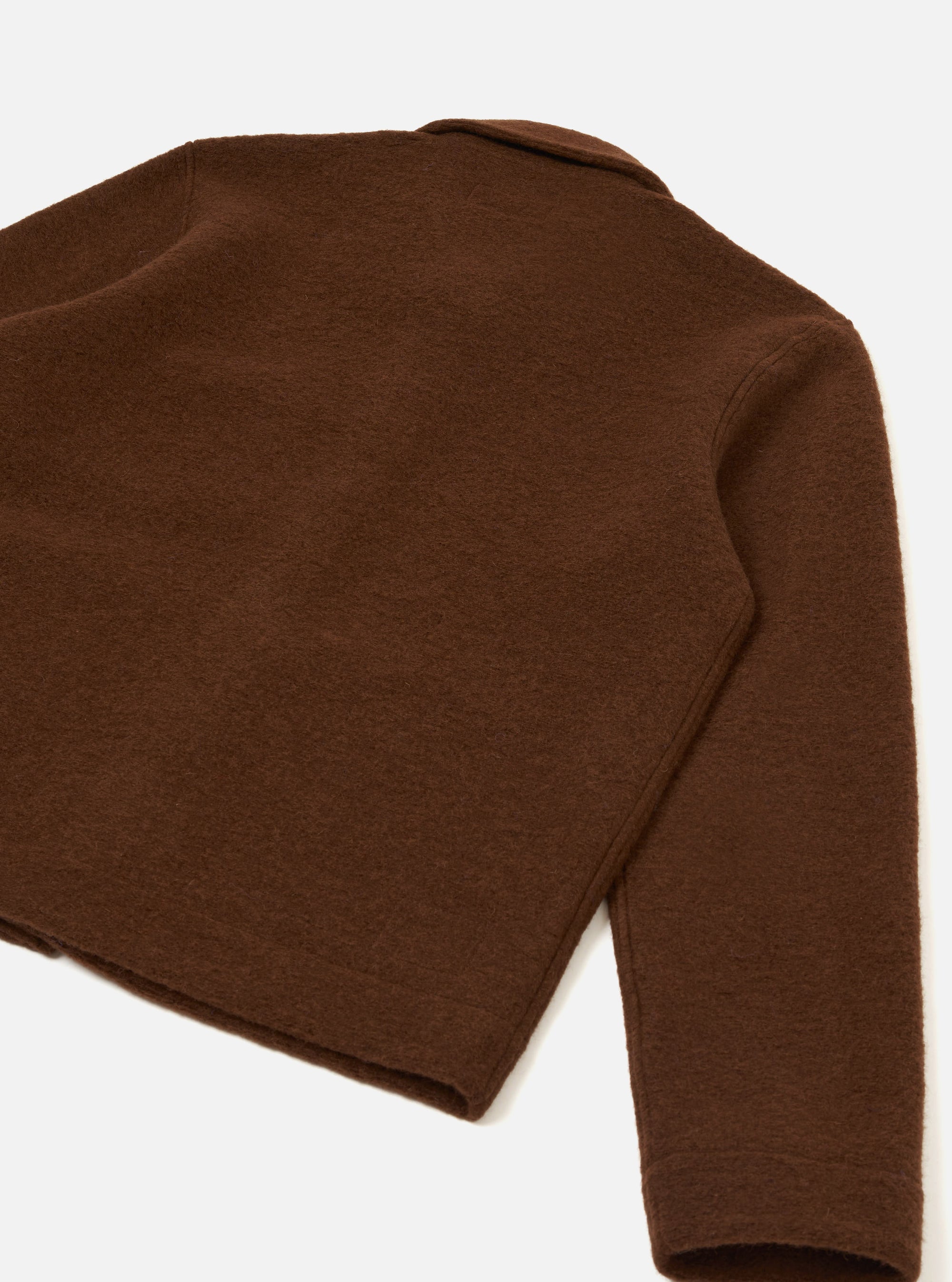 Back view of a cacao brown wool fleece uniform jacket, laid flat on a light grey seamless surface. The shot is cropped to show the upper back, one full sleeve with a plain cuff, and a partial collar visible at the top. The boiled wool texture is visible across the body and sleeve.