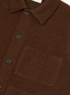 Close-up of a cacao wool fleece uniform jacket on a plain white backdrop. The shot shows the spread collar, button placket with dark four-hole buttons, and a patch pocket on the chest. The brushed wool fleece texture is clearly visible across the body.