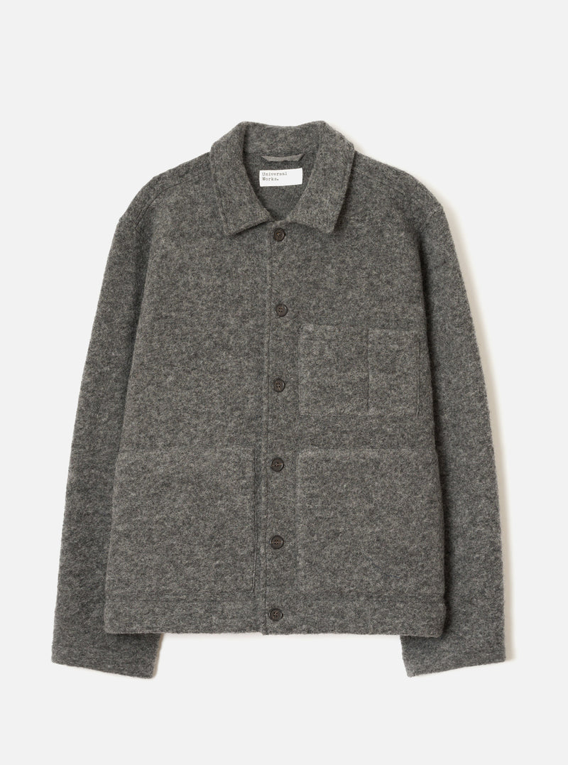 Grey marl wool fleece uniform jacket laid flat on a light grey seamless backdrop. Spread collar with a Universal Works woven label at the neckline. Five dark buttons run down the centre front placket. One chest patch pocket and two large lower patch pockets. Full-length sleeves with plain cuffs. Textured boiled wool fleece fabric throughout.