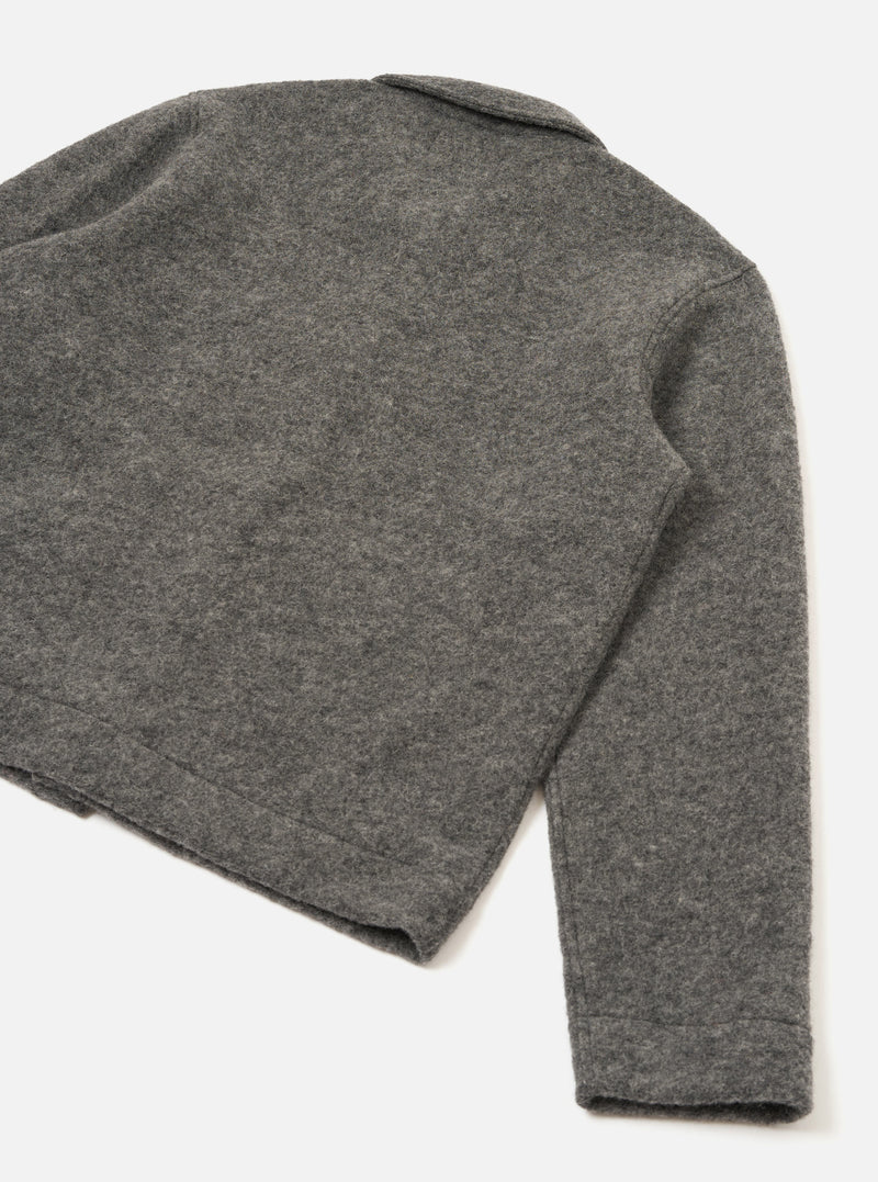 Close-up flat lay of a grey marl wool fleece uniform jacket on a white studio surface, shot from above at an angle. The back panel and one sleeve are visible, showing the soft, lightly textured boiled wool fleece fabric. A small collar is visible at the top. The sleeve ends in a plain, clean-finished cuff.