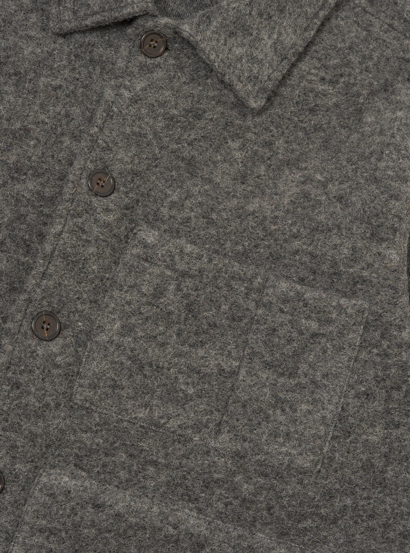 Close-up of a grey marl wool fleece uniform jacket on a plain white backdrop. The shot shows the spread collar, three dark horn-effect buttons on the placket, and a large patch pocket visible on the chest. The brushed, fleecy wool texture is prominent across the fabric.